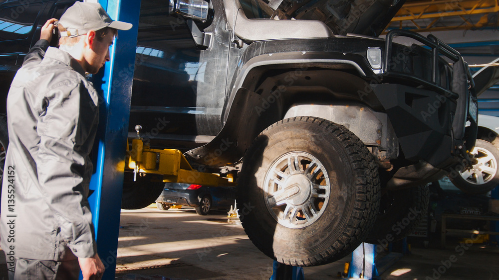 Fototapeta premium Mechanic lifts SUV in garage automobile service