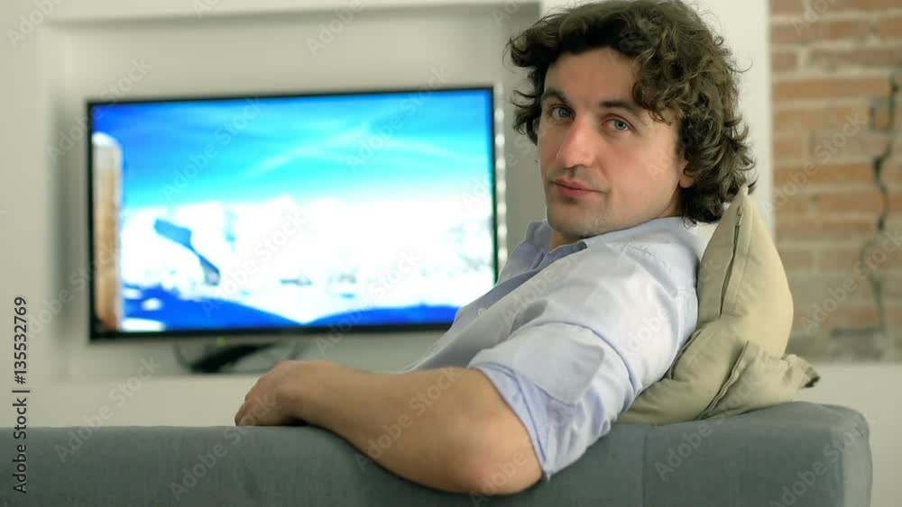 Man watching television and looking to the camera while relaxing on the sofa
Man watching television and looking to the camera while relaxing on the sofa