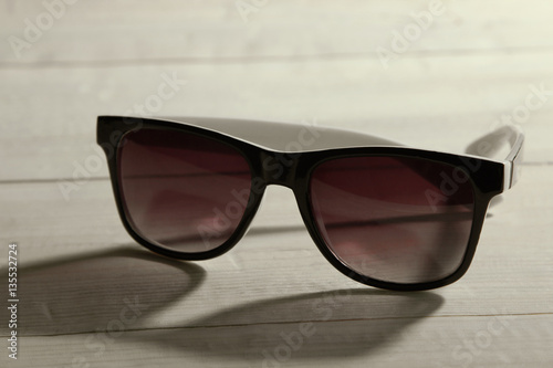 The black sunglasses lying on a white wooden background.