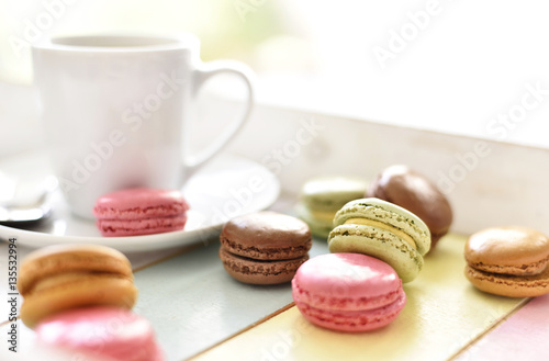 Delicious colorful macarons with cream and coffee cup. Coffee break scene with macaron candy and selective focus.