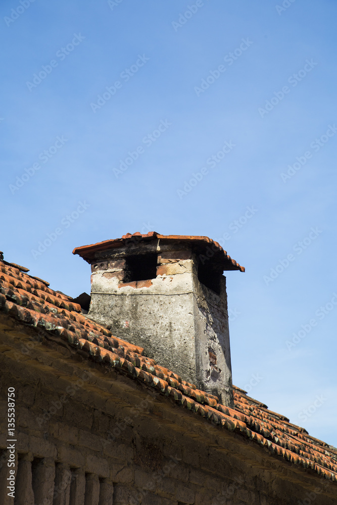 Close up of a brick chimney on tile roof against blue sky Close up of a brick chimney on tile roof against blue sky