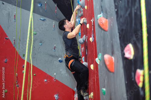 Young man climbing indoor wall and reaching the top