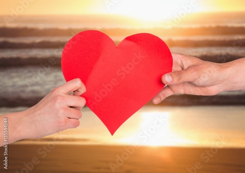 Hands of couple holding red heart on beach