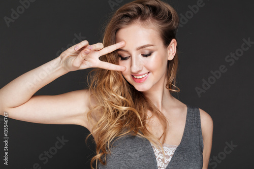 Cheerful lady posing over dark background make peace gesture.