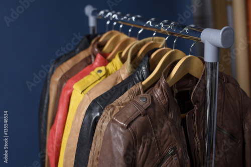 Many colored leather jacket hanging on rack on blue background