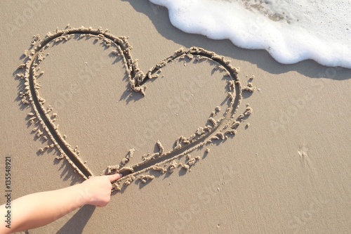 woman drawing a heart in the sand on beach, sunset time. Valentine's concept.