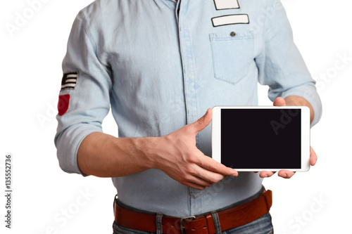 A man in a light blue shirt and jeans with a brown belt is holding tablet pc isolated on white background