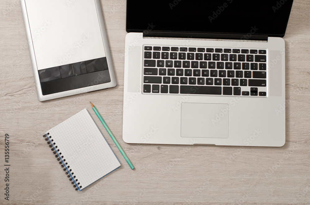Open the laptop, graphics tablet and notebook with pencil on a light table, top view Open the laptop, graphics tablet and notebook with pencil on a light table, top view
