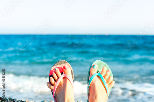 Summertime enjoyment! Lady's feet on the beach. Ocean waves back