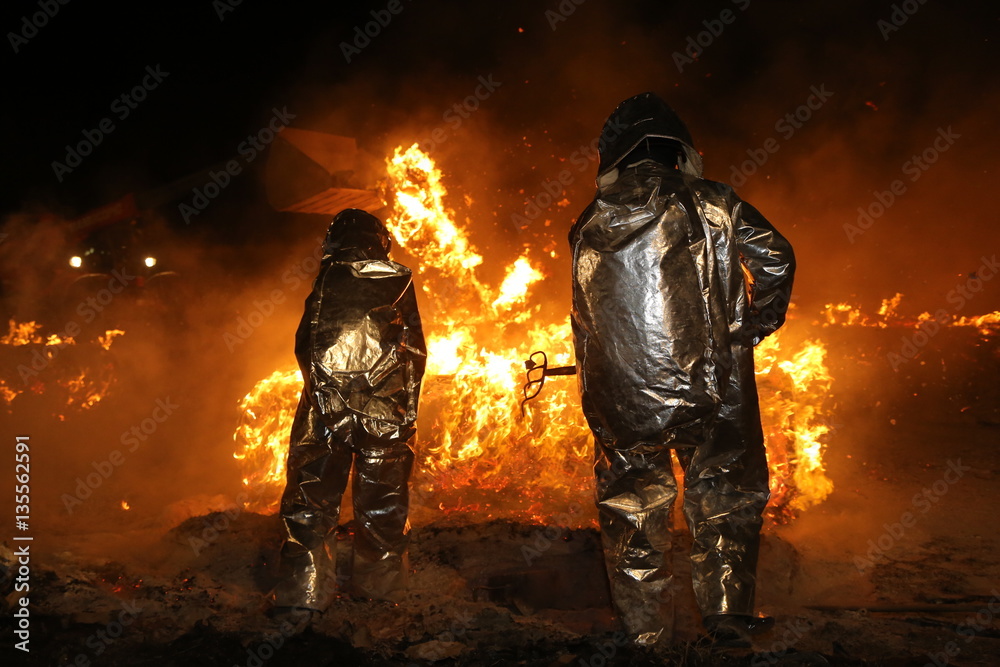 Naklejka premium Feuerwehrmänner in Schutzkleidung lösen brennende Teile aus einem Brandherd heraus damit das Feuer besser gelöscht werden kann