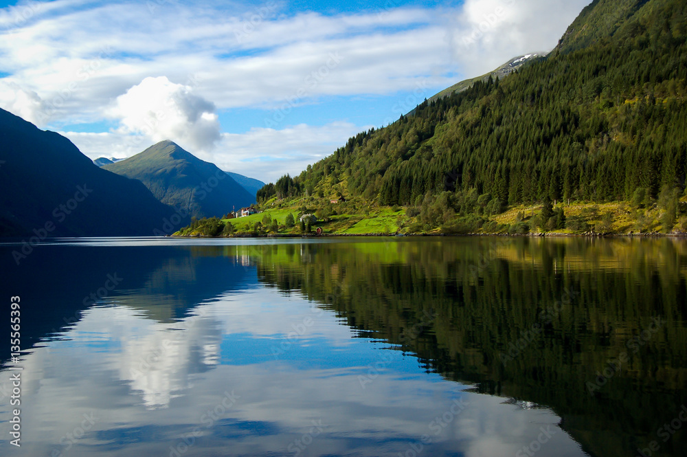 gudvangen fjord in norway refleting on the water on a blue sky with clouds background