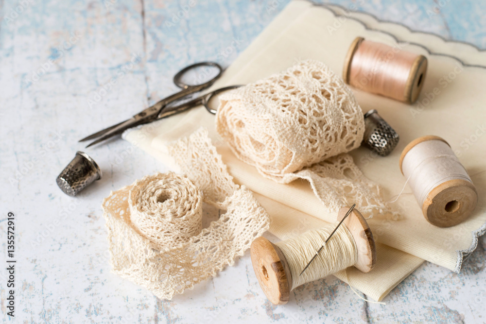 
 Sewing supplies and accessories for needlework.
 Fabric, openwork lace, spools of thread, scissors and thimbles on an old wooden table. - obrazy, fototapety, plakaty 