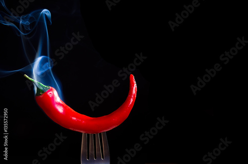 smoking chili pepper on fork on black background