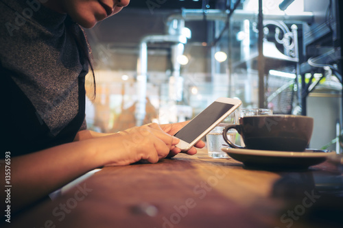 A woman using smartphone and drinking coffee in cafe