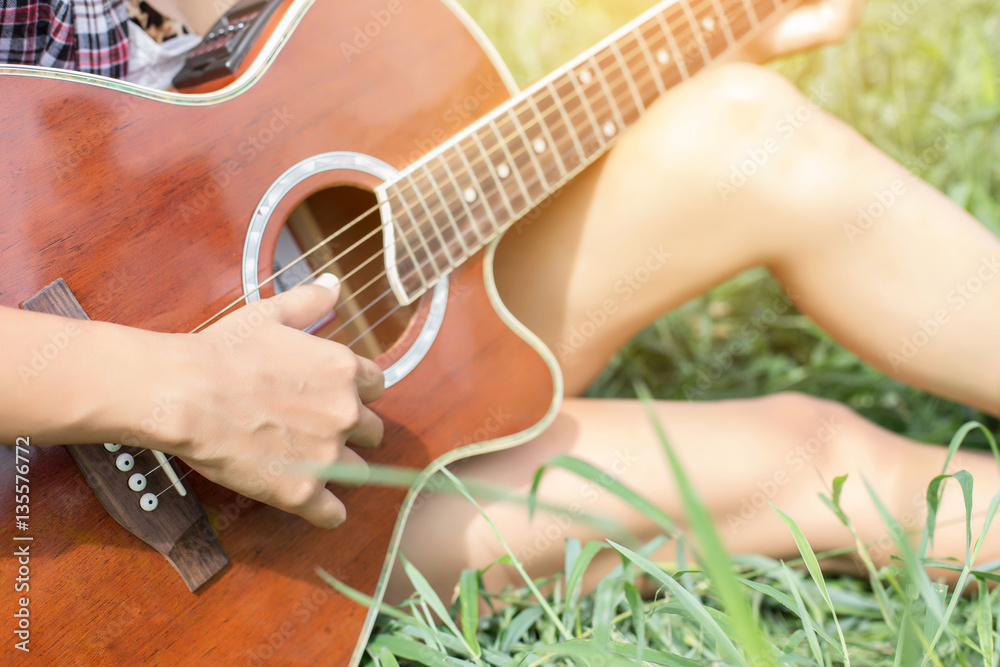 Fototapeta premium Young hipster girl sitting playing a guitar and singing.