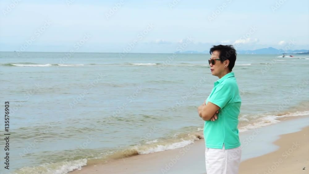 Asian senior woman wearing sunglasses and thinking about life planning next to the sea Asian senior woman wearing sunglasses and thinking about life planning next to the sea