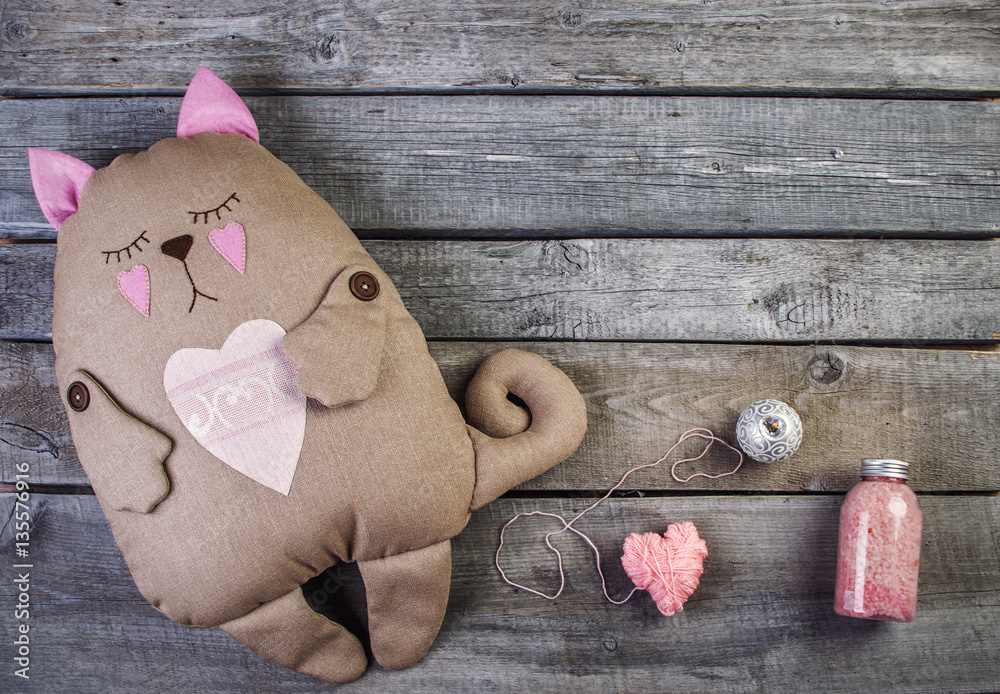 wooden background with soft toy cat and pink heats and candle f