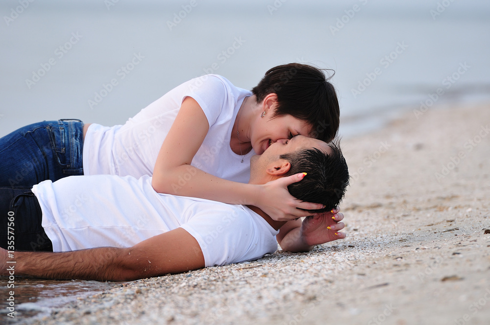 Happy in the arms of a young couple lying on the sand beach