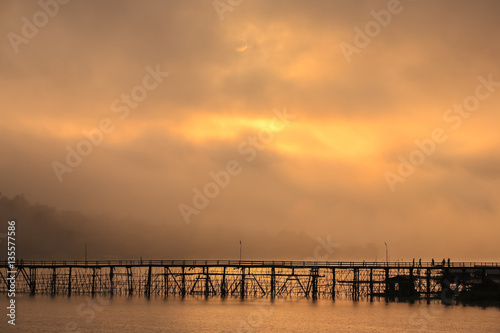 Wooden bridge across gold river with foggy background located at kanchanaburi province thailand