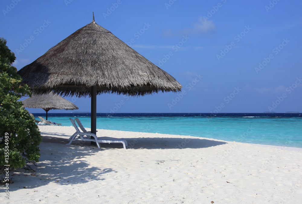 Beach umbrellas made of straw and sunbeds in the secluded beach, Maldives
