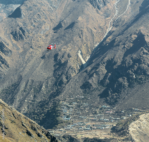 The helicopter flies to the background of the village Phortse - Nepal photo