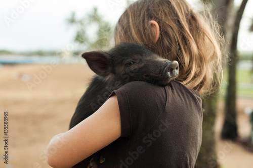 Young child carrying black piglet 