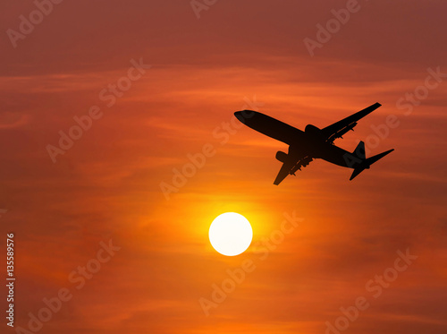  Silhouette passenger airplane flying away in to sky high altitude above the sun during sunset