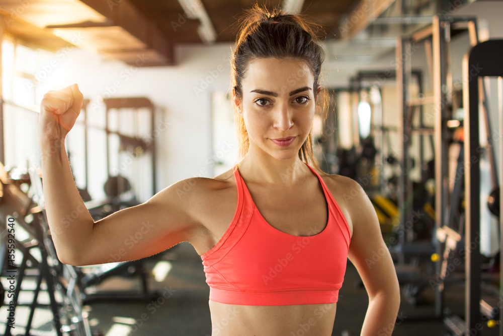 Sporty woman showing her biceps in gym.