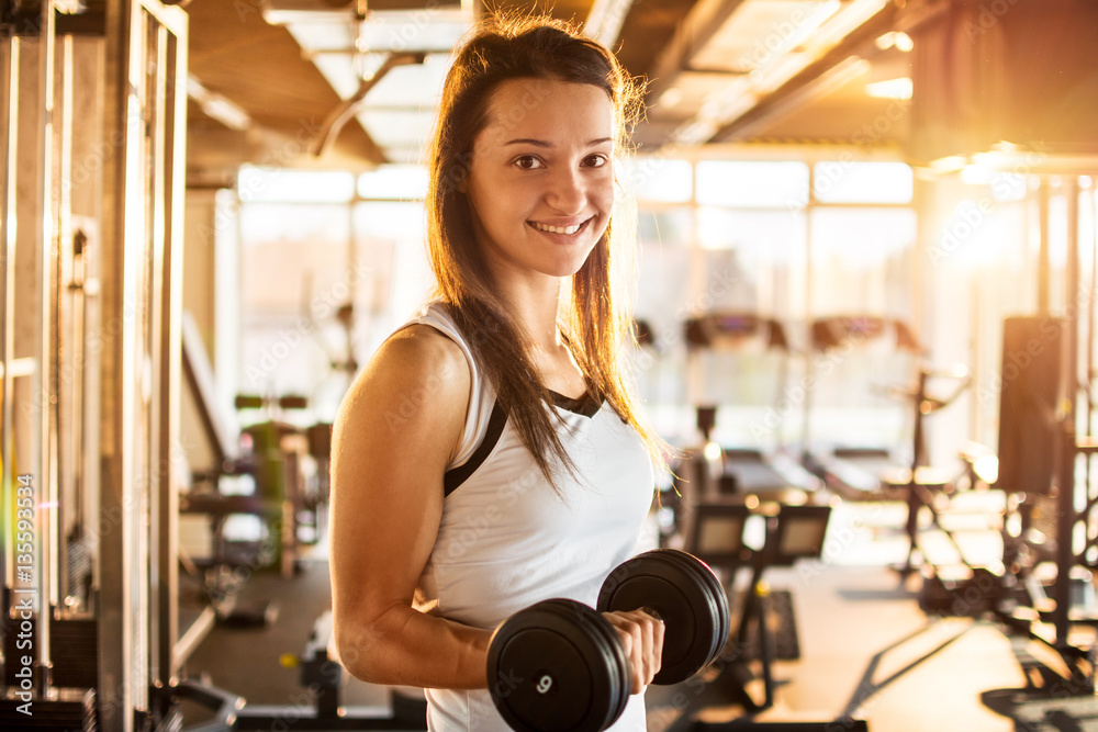 Young sporty woman lifting steel dumbbell in gym. Young sporty woman lifting steel dumbbell in gym.