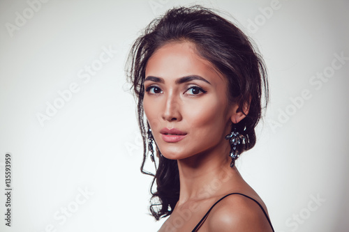 Glamour portrait of beautiful woman with earrings and fresh daily makeup on grey background.