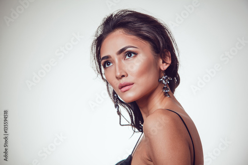 Glamour portrait of beautiful woman with earrings and fresh daily makeup on grey background.