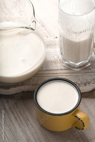Glass and pitcher of kefir and yellow cup on a white stand