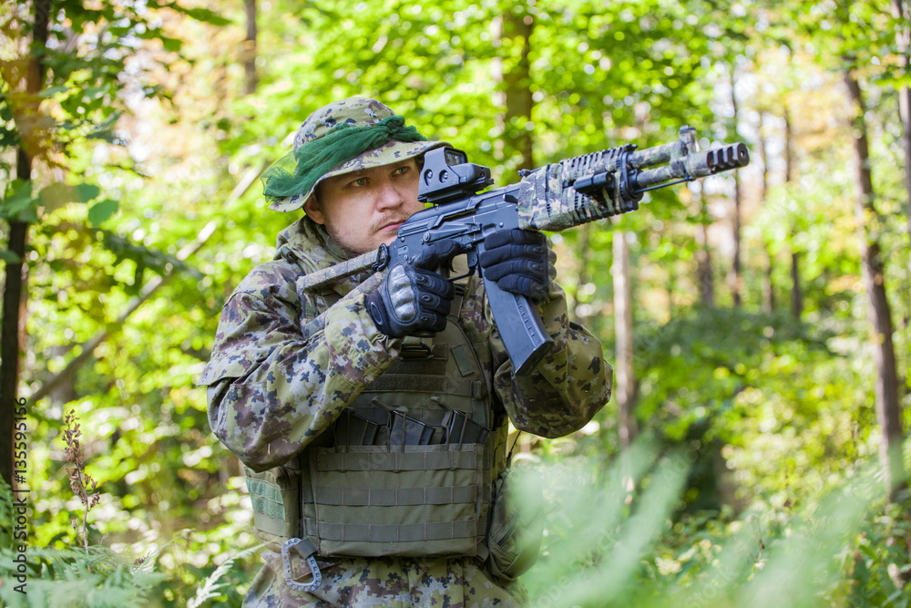 Military man in camouflage uniforms and flak jacket with a gun in the woods