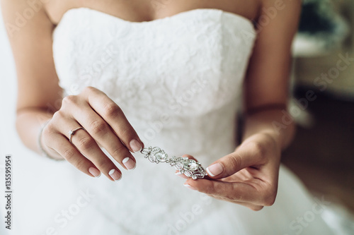 Elegant bride holding silver earrings. Tender hands with jewelry.