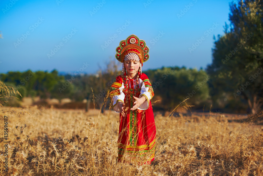 Beautiful girl in Russian folk costume touching wheat