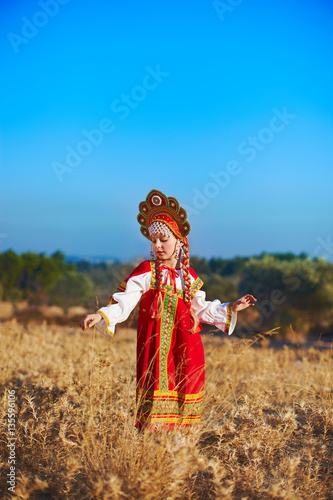 Beautiful girl in Russian folk costume dancing at field