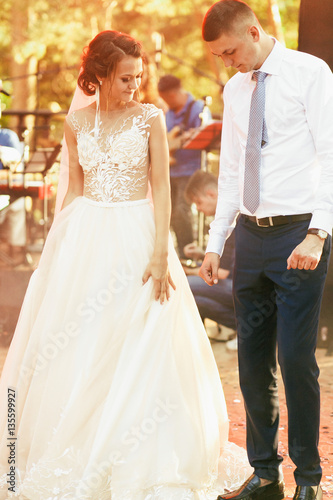 Yellow rays of evening sun shine over happy wedding couple stand © IVASHstudio