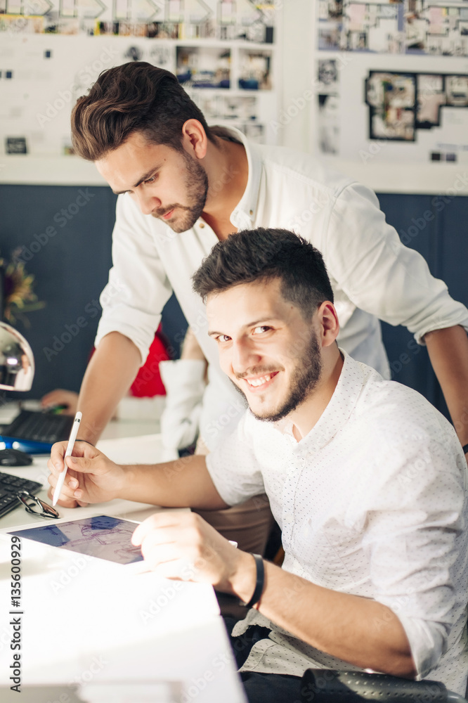 Fototapeta premium Two designer drawing sketches and looking at tablet screen.