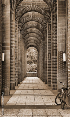 A bike Leaning on the front part of an arch corridor. There are two street lamps fixed on the arch. Sepia tone. photo