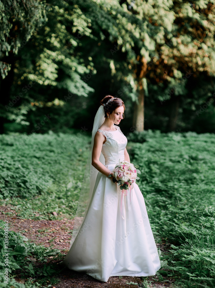 Wonderful bride stands on the path in forest with closed eyes