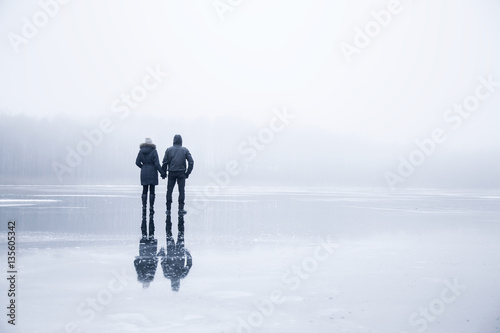 Couple in the mist walking on the lake ice in winter afternoon. Peaceful atmosphere. Foggy air.