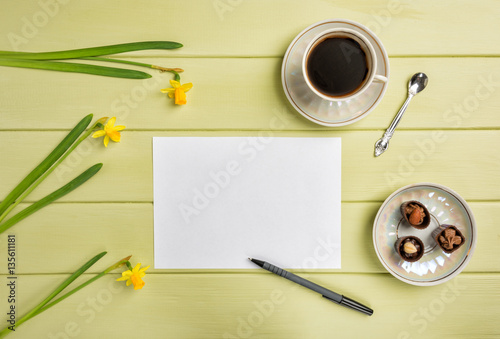 Paper, a pen, cup of black coffee and flowers on a wooden background. Top view. Copy space. © markovael