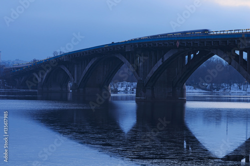Frosty early morning. Metro bridge reflected in the water. The first metro train moves on the bridge. Kyiv. Ukraine