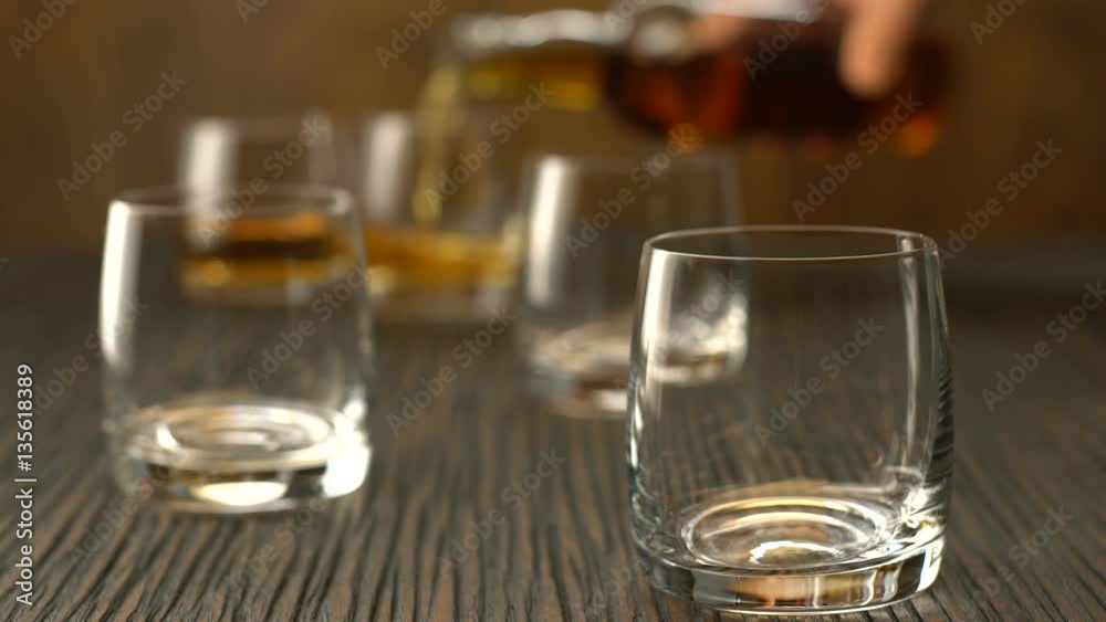 Pouring whiskey into the glass on a wooden table Pouring whiskey into the glass on a wooden table