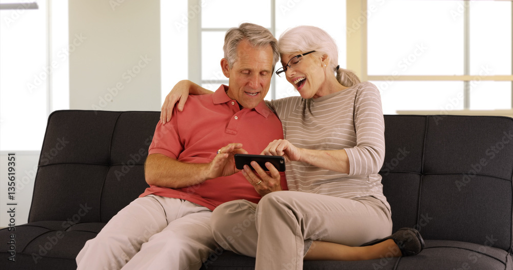 Modern Seniors sitting on couch watching videos on smartphone Modern Seniors sitting on couch watching videos on smartphone