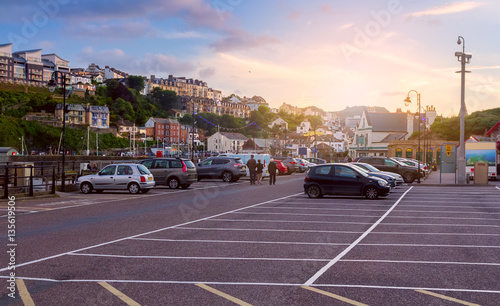 Car parking at the harbor in the town of Ilfracombe. Walking people. Many houses on the hill.  North Devon. UK