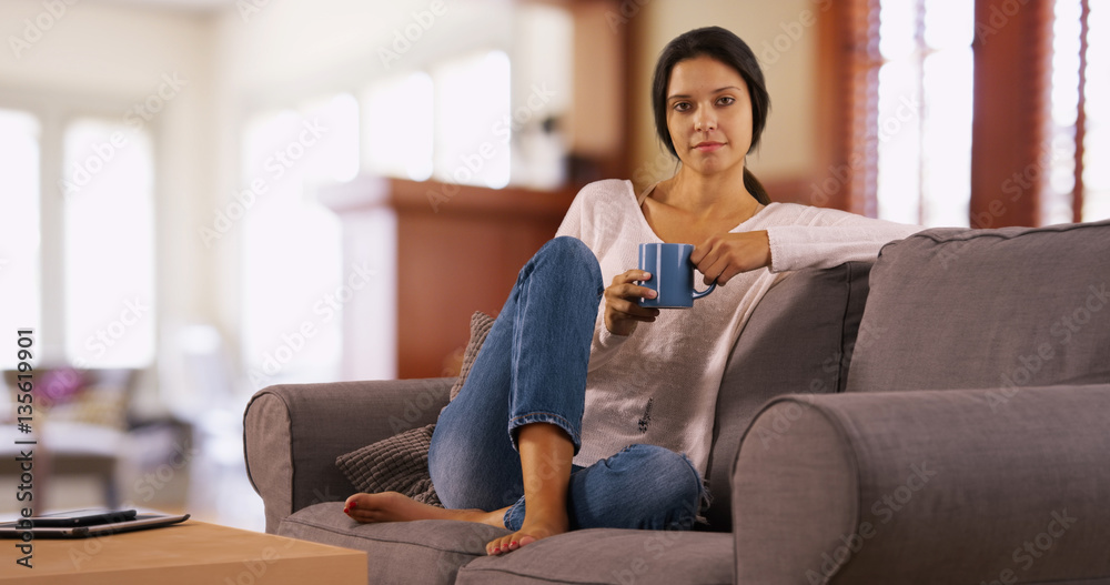 Millennial white woman poses on her couch holding her coffee