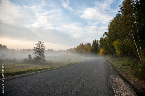 misty countryside landscape with asphalt wavy road in latvia