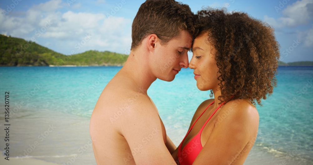 Close up of mixed race couple cuddling together on tropical beach. Close up of mixed race couple cuddling together on tropical beach.