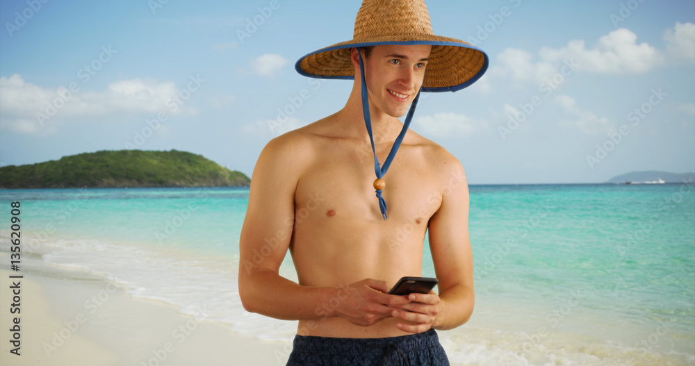 Caucasian male texting on cell phone from Caribbean shore.